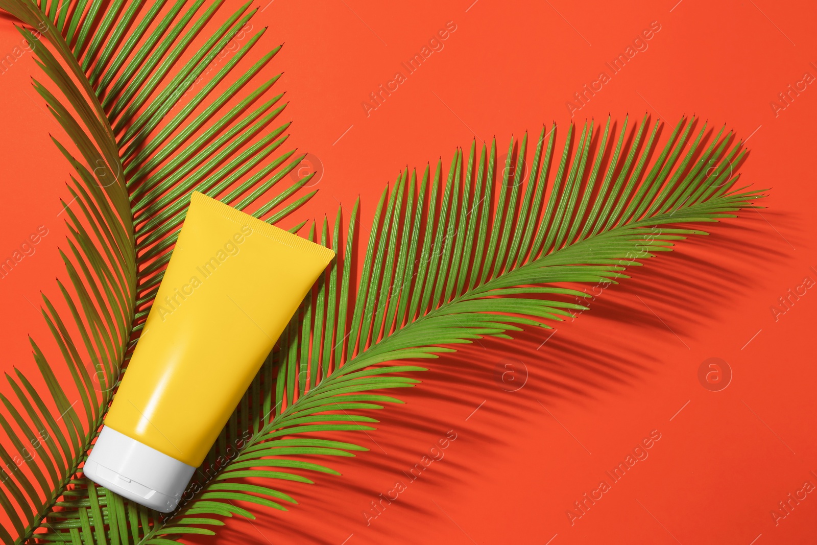 Photo of Sunscreen and tropical leaves on coral background, flat lay. Sun protection care
