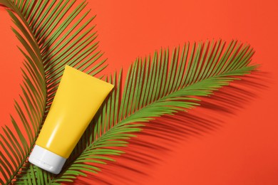 Sunscreen and tropical leaves on coral background, flat lay. Sun protection care