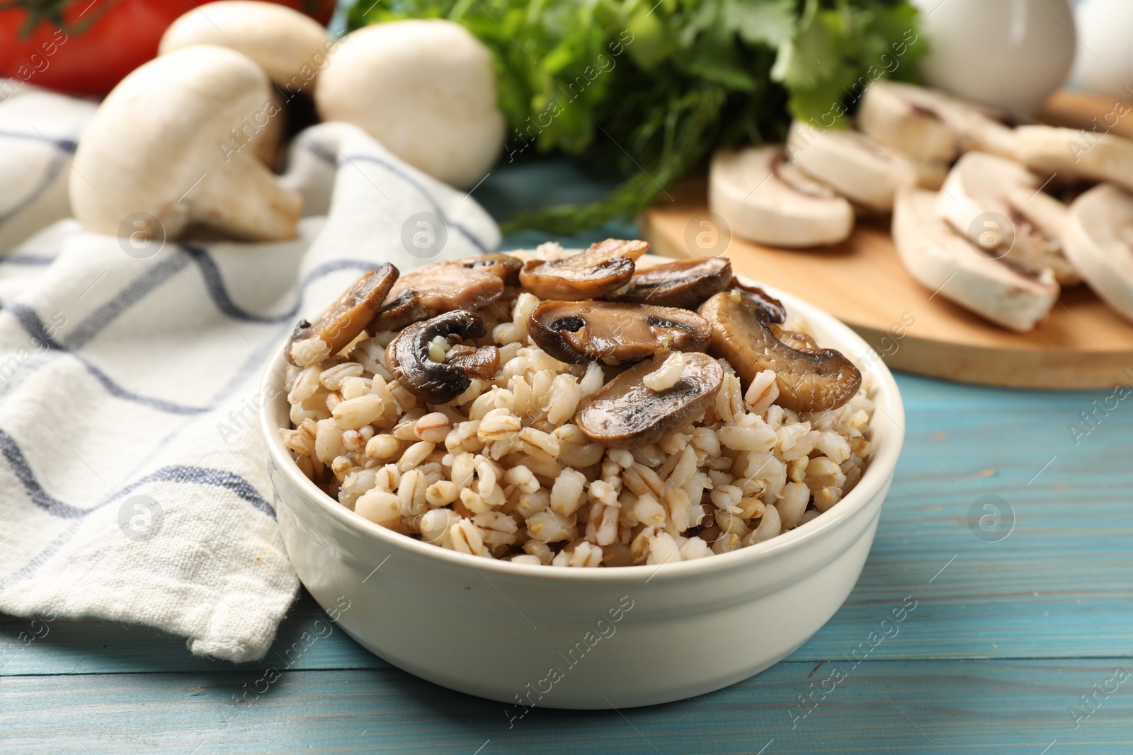 Photo of Delicious pearl barley with mushrooms in bowl on light blue wooden table, closeup