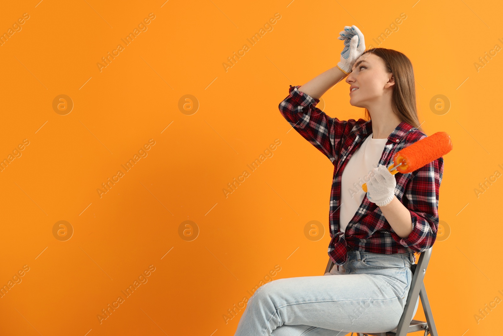 Photo of Designer with roller sitting on folding ladder near freshly painted orange wall, space for text