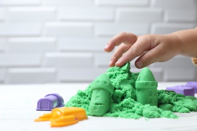Little child playing with green kinetic sand at white table, closeup. Space for text