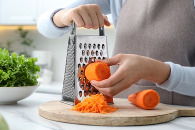 Photo of Woman grating fresh ripe carrot at kitchen table, closeup