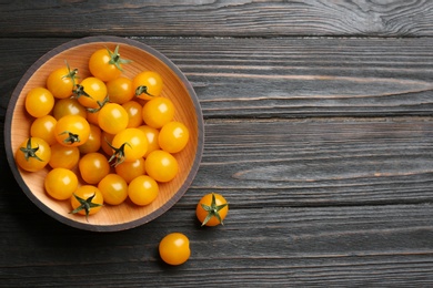 Photo of Ripe yellow tomatoes in bowl on dark wooden table, flat lay. Space for text