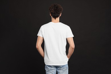 Photo of Man wearing white t-shirt on black background, back view. Mockup for design