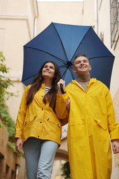Photo of Lovely young couple with umbrella walking under rain on city street, low angle view