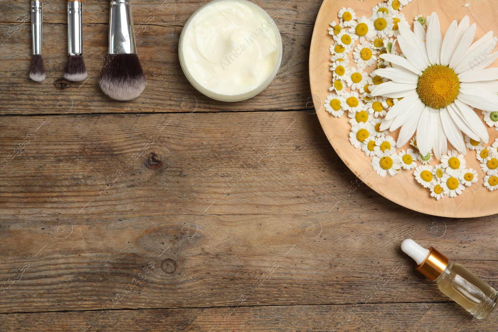 Photo of Flat lay composition with chamomile flowers and cosmetic products on wooden table, space for text