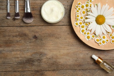Photo of Flat lay composition with chamomile flowers and cosmetic products on wooden table, space for text