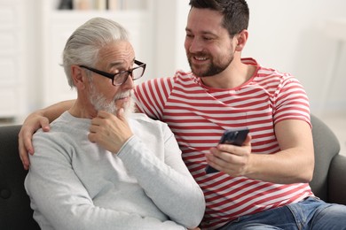 Photo of Happy son and his dad watching something on smartphone at home