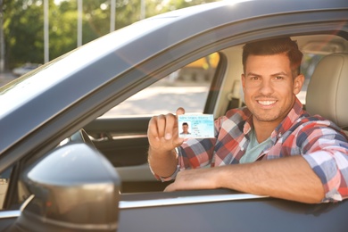 Photo of Happy man holding license while sitting in car outdoors. Driving school