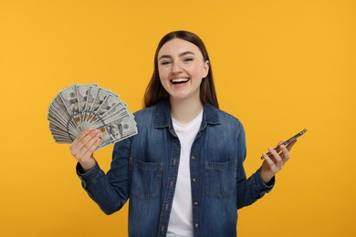 Photo of Happy woman with dollar banknotes and smartphone on orange background