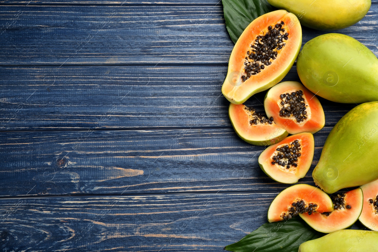 Photo of Fresh ripe papaya fruits with green leaves on blue wooden table, flat lay. Space for text