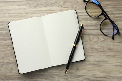 Photo of Open notebook, pen and glasses on wooden table, flat lay. Space for text