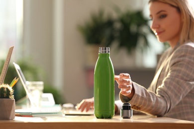 Photo of Woman taking green thermos bottle at workplace, closeup