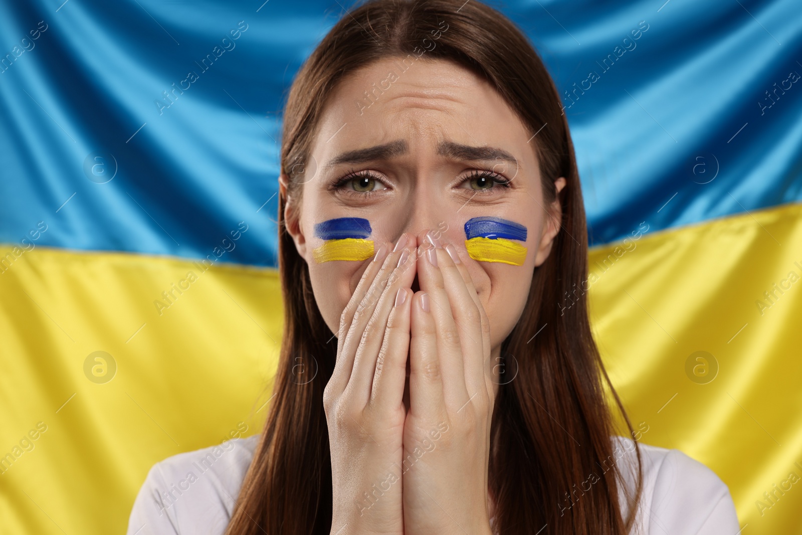 Photo of Sad young woman with clasped hands near Ukrainian flag