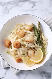 Photo of Delicious scallop pasta with asparagus and lemon on white marble table, top view