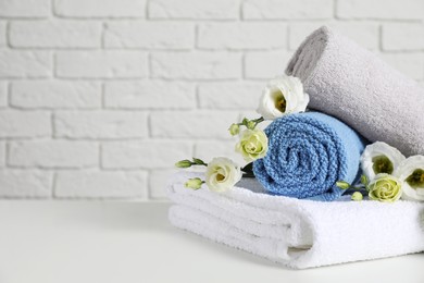 Clean soft towels with flowers on table near white brick wall. Space for text
