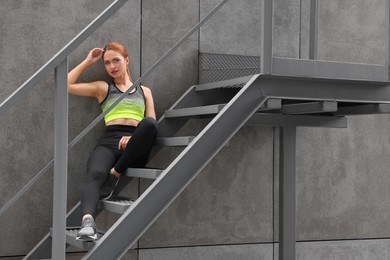 Beautiful woman in stylish gym clothes sitting on stairs on street