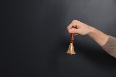 Teacher with school bell near black chalkboard, closeup. Space for text