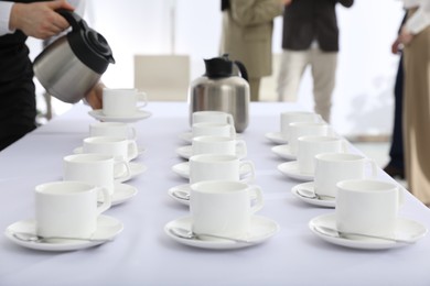 Waitress pouring hot drink during coffee break, focus on table with cups