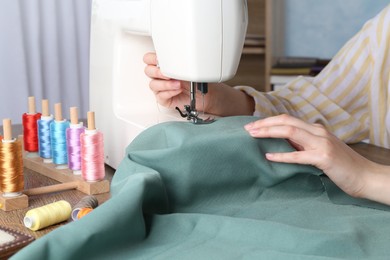 Seamstress working with sewing machine at wooden table indoors, closeup