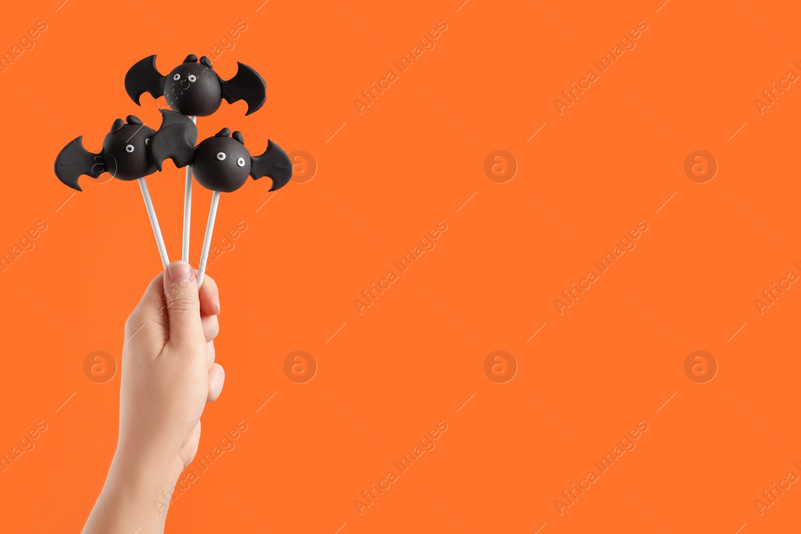 Photo of Woman with delicious bat shaped cake pops and space for text on orange background, closeup. Halloween celebration