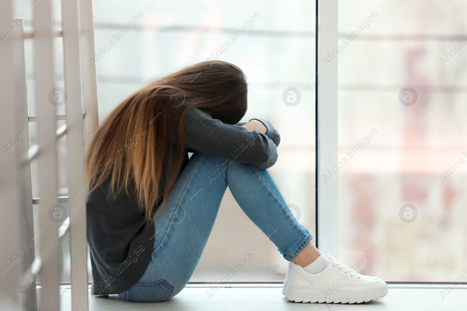 Photo of Upset teenage girl sitting at window indoors. Space for text