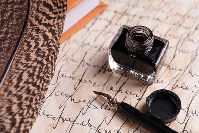 Open inkwell, fountain pen, feather and book on vintage parchment with text, closeup