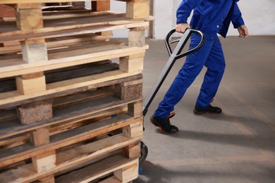 Worker moving wooden pallets with manual forklift in warehouse, closeup