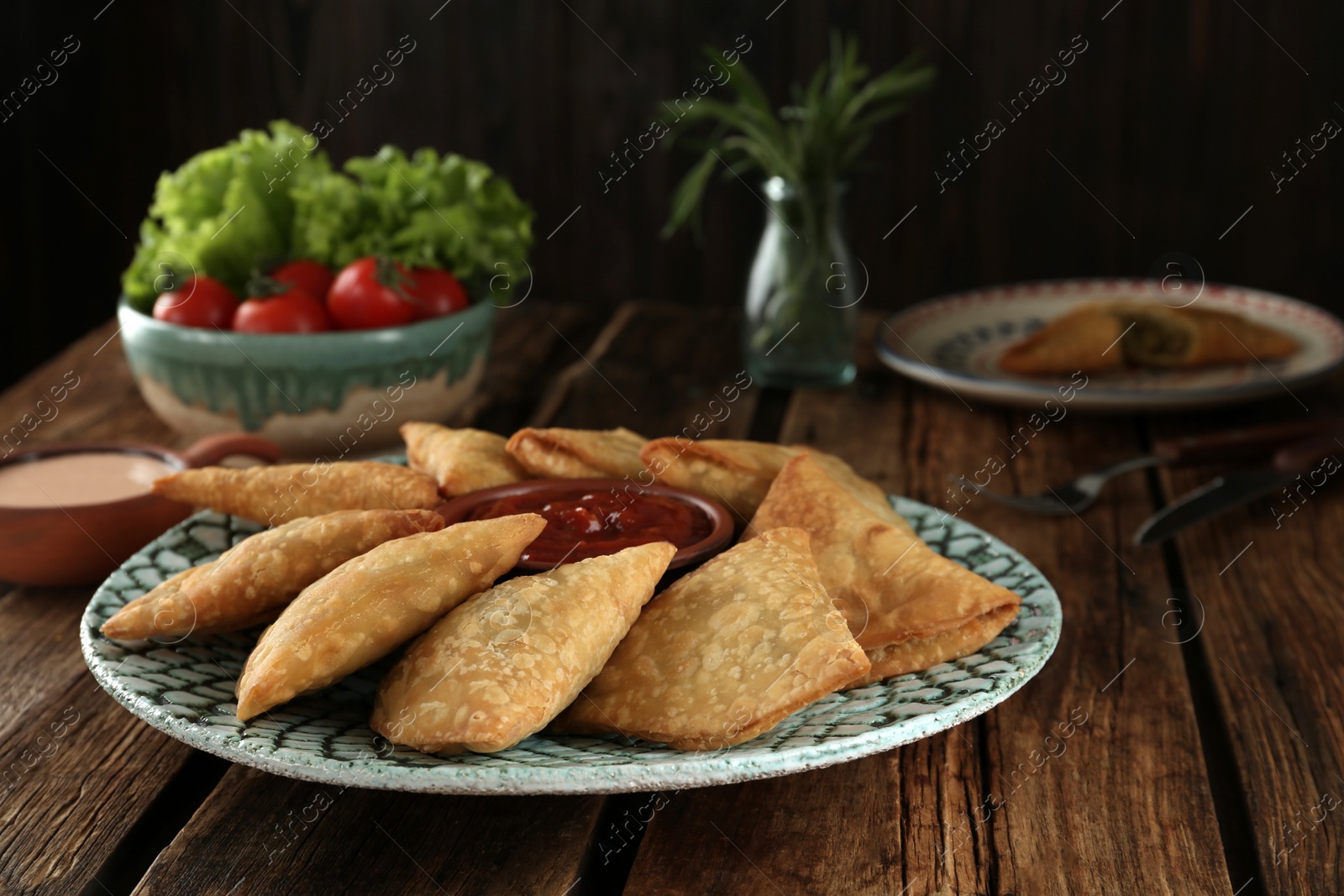 Photo of Delicious samosas with sauce on wooden table, closeup