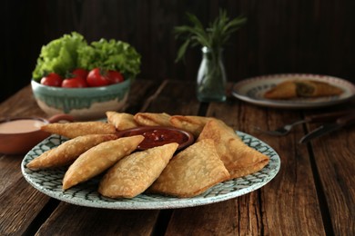 Delicious samosas with sauce on wooden table, closeup