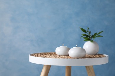 Burning candles and plant on white table against light blue background, space for text