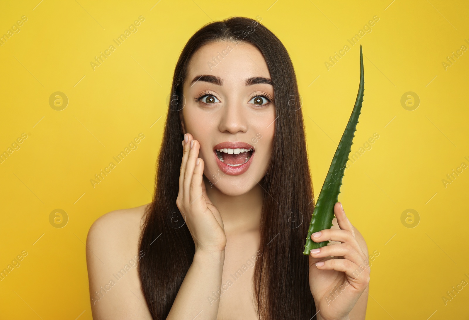 Photo of Emotional young woman with aloe vera leaf on yellow background