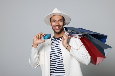 Photo of Happy African American man in hat with shopping bags and credit card on light grey background