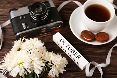 Photo of Beautiful composition with white chrysanthemum flowers and vintage camera on wooden table