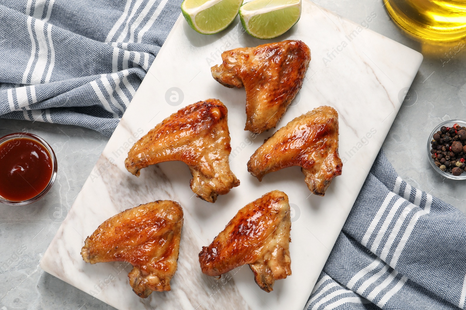 Photo of Delicious fried chicken wings on white marble board, flat lay