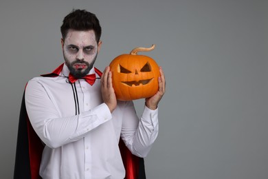 Photo of Man in scary vampire costume with fangs and carved pumpkin on light grey background, space for text. Halloween celebration