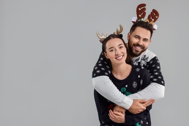 Photo of Happy young couple in Christmas sweaters and reindeer headbands on grey background. Space for text