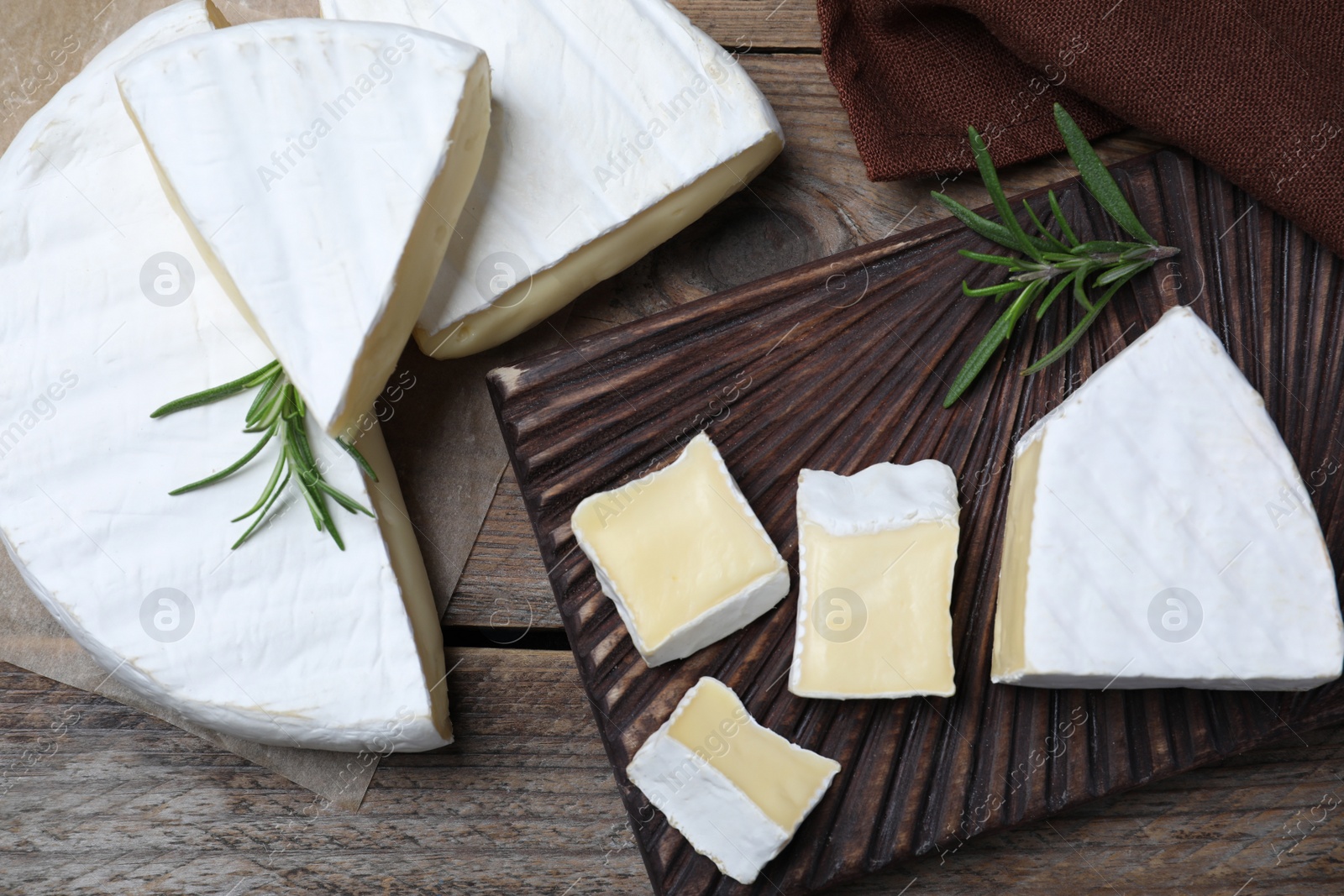 Photo of Tasty cut brie cheese with rosemary on wooden table, flat lay
