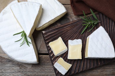 Tasty cut brie cheese with rosemary on wooden table, flat lay