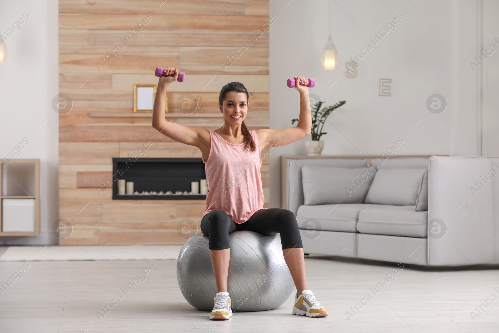 Photo of Young woman doing exercise with dumbbells on fitness ball at home