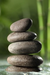 Photo of Stacked stones on water surface against bamboo stems and green leaves, closeup