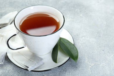 Photo of Aromatic tea in cup, teabags and green leaves on grey table