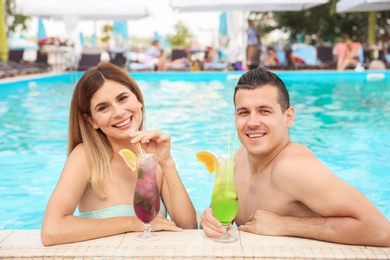 Happy couple with cocktails resting in blue swimming pool outdoors