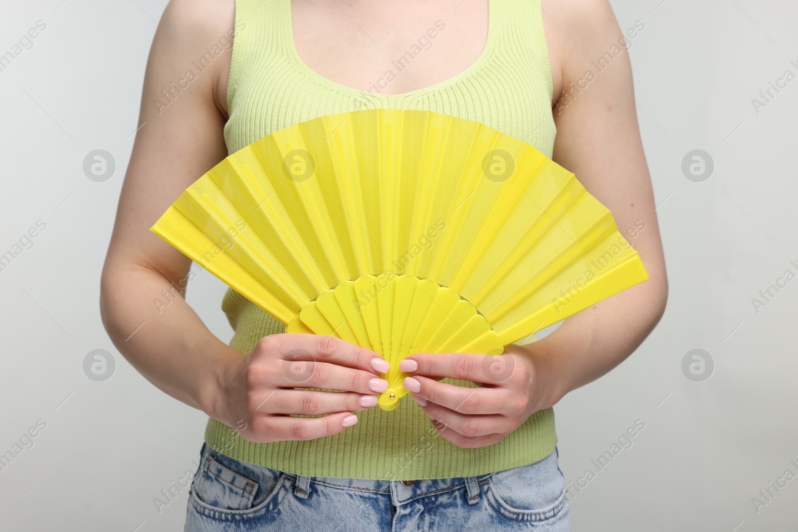 Photo of Woman with yellow hand fan on light grey background, closeup