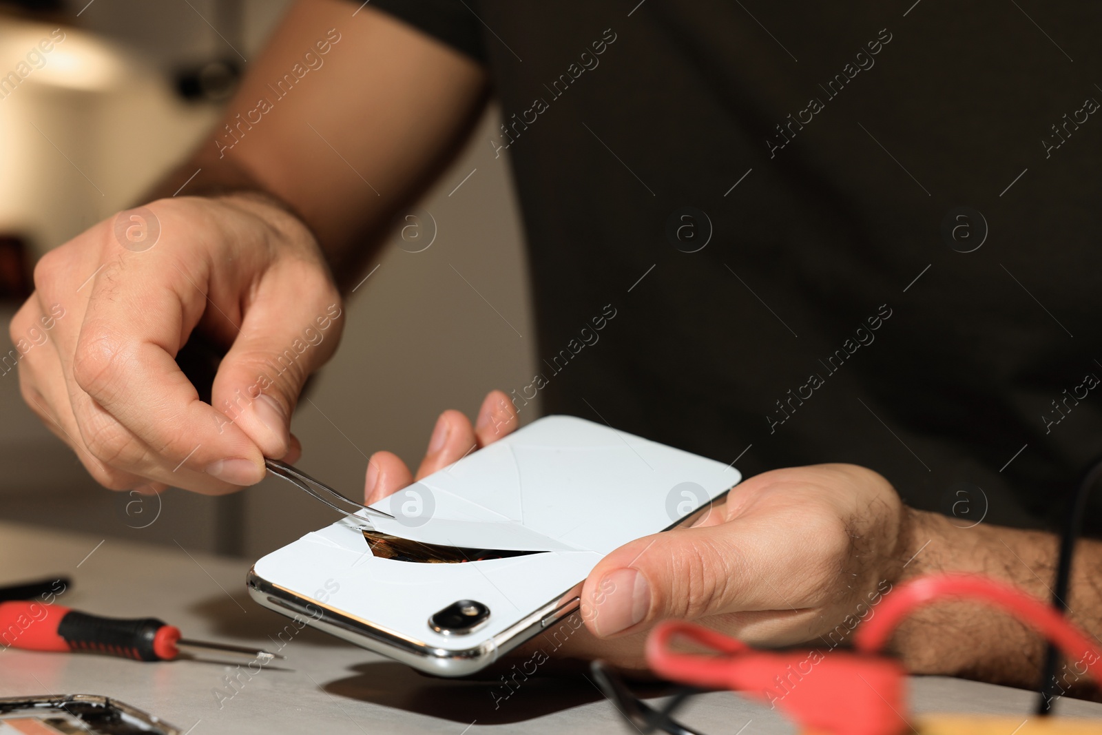 Photo of Technician repairing broken smartphone at table, closeup