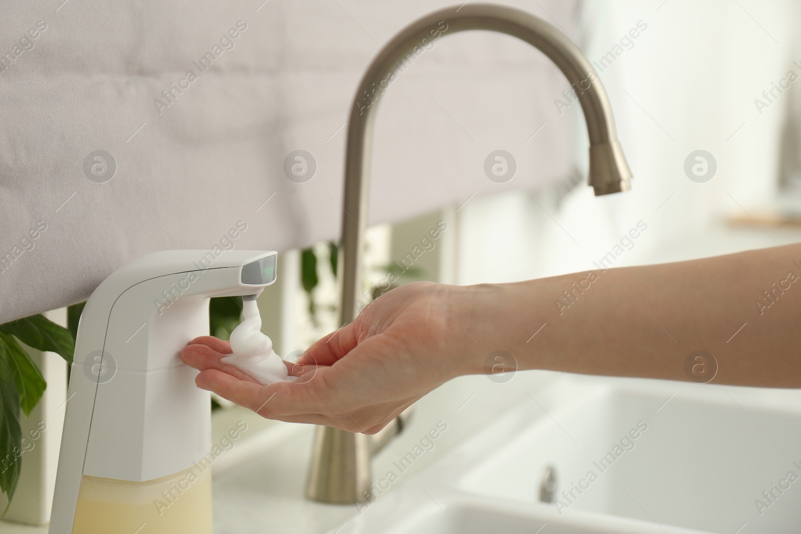 Photo of Woman using automatic soap dispenser in kitchen, closeup