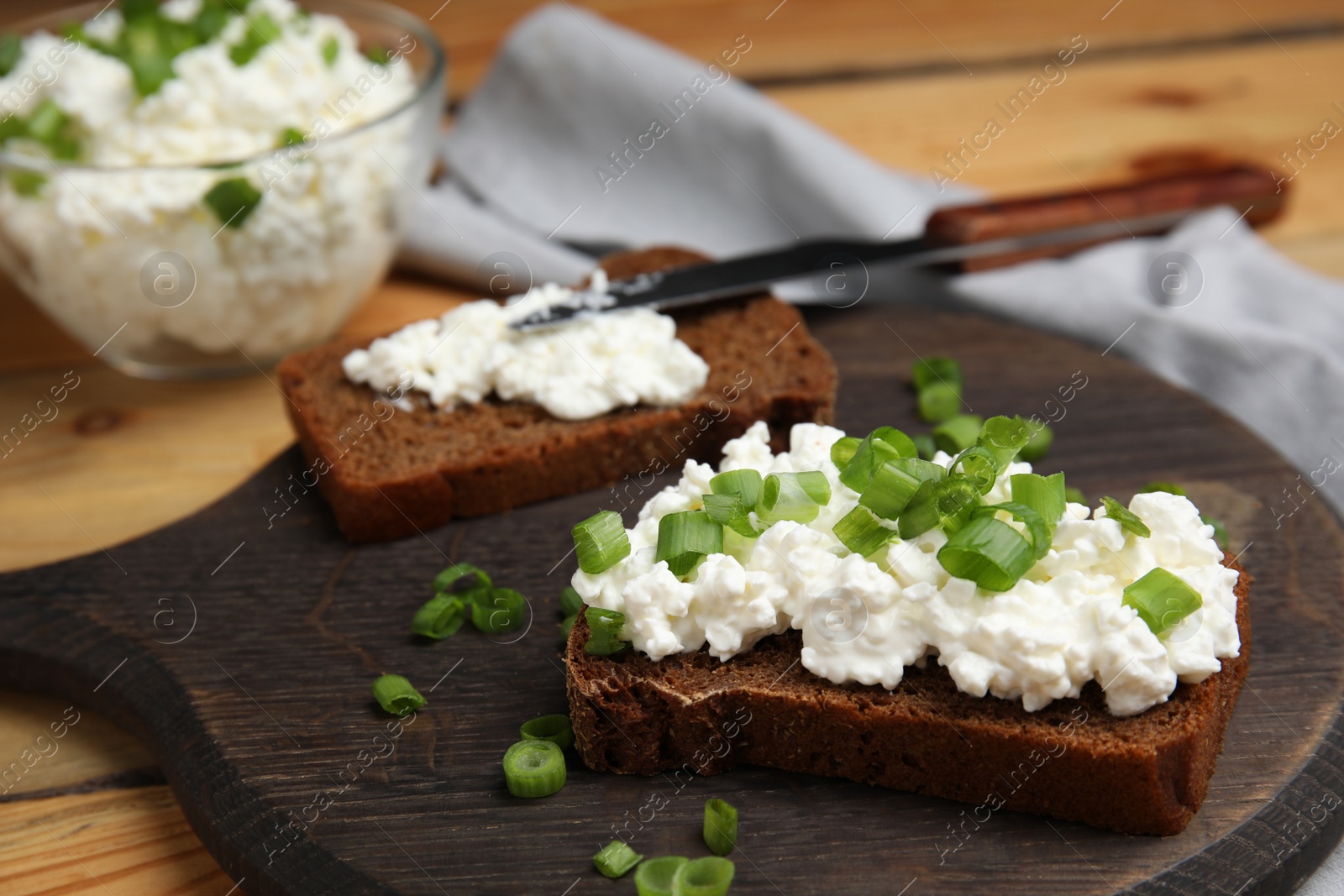 Photo of Bread with cottage cheese and green onion on wooden table, closeup