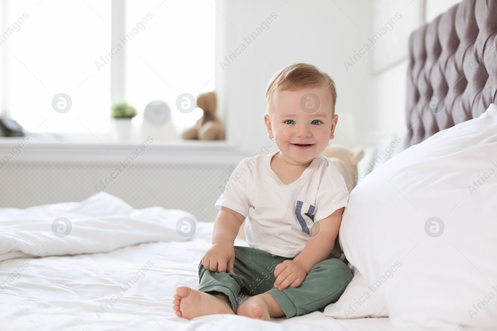 Photo of Adorable little baby sitting on bed at home