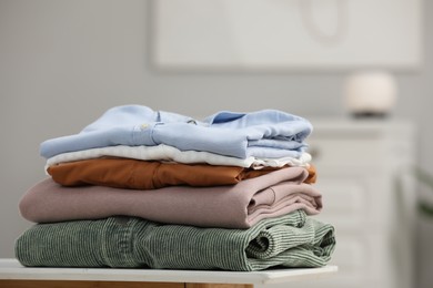 Photo of Stack of different folded clothes on bedside table indoors, closeup