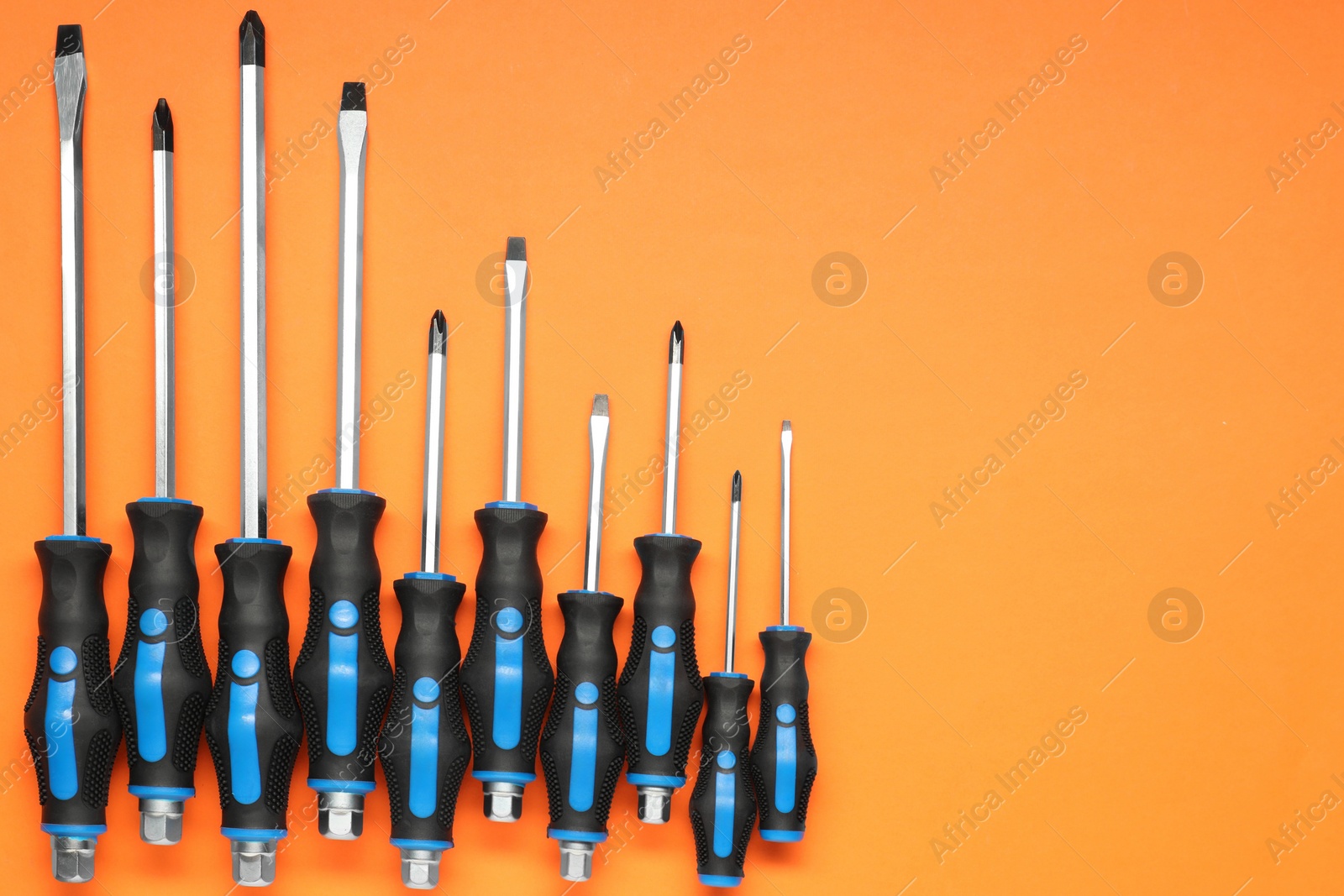 Photo of Set of screwdrivers on orange background, flat lay. Space for text
